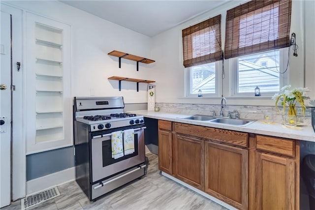 kitchen featuring stainless steel gas range, brown cabinets, a sink, light countertops, and visible vents