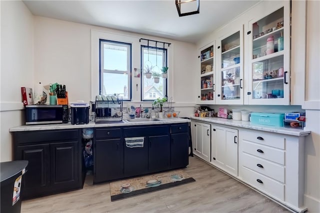 kitchen featuring white cabinets, a sink, light wood finished floors, light countertops, and stainless steel microwave