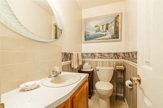 half bathroom featuring vanity, toilet, tile patterned floors, and a wainscoted wall