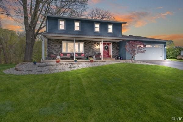 traditional home with an attached garage, stone siding, concrete driveway, a porch, and a yard