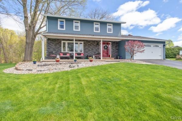 traditional-style home featuring a front lawn, stone siding, a garage, covered porch, and driveway