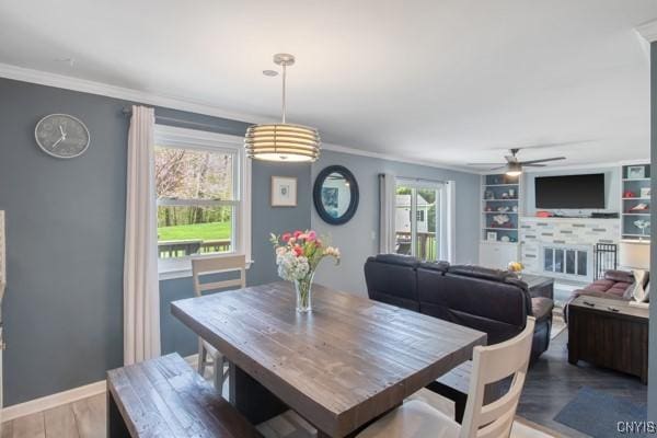 dining area featuring crown molding, a ceiling fan, a glass covered fireplace, and wood finished floors