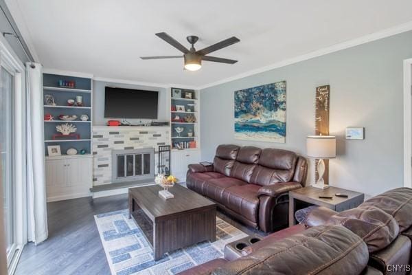 living room with ceiling fan, crown molding, a fireplace, built in shelves, and wood finished floors