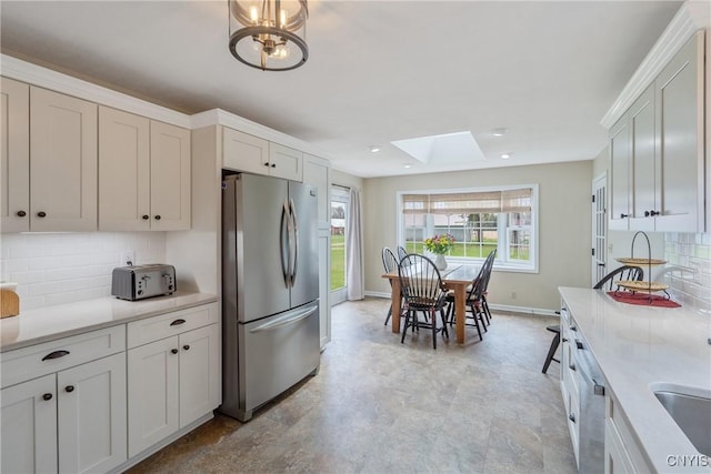 kitchen featuring freestanding refrigerator, baseboards, light countertops, backsplash, and a skylight