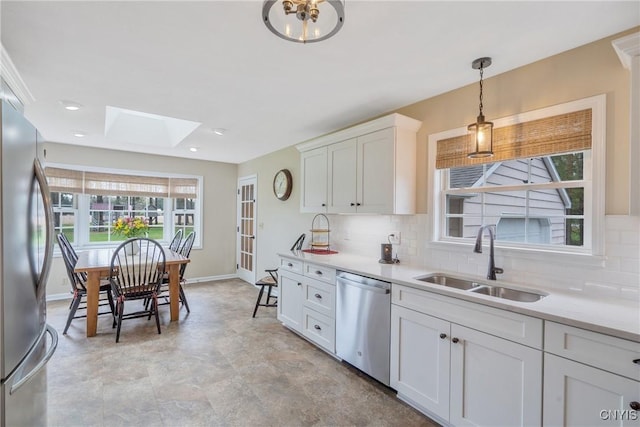kitchen featuring a skylight, tasteful backsplash, a sink, baseboards, and stainless steel appliances