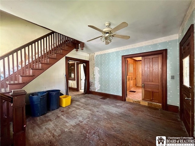 unfurnished living room with stairs, a ceiling fan, wallpapered walls, baseboards, and wood finished floors