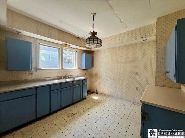 kitchen with light floors, blue cabinets, a sink, and wallpapered walls