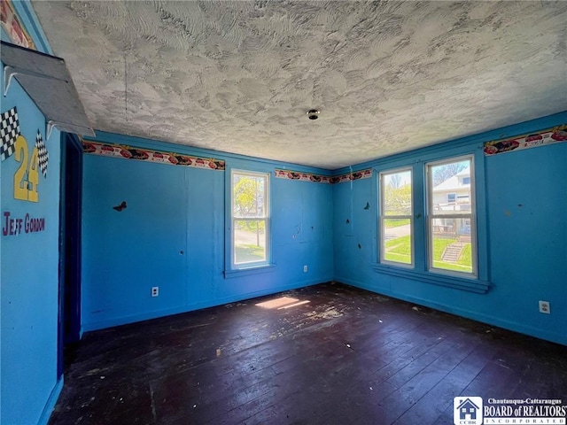 unfurnished room with wood-type flooring, a textured ceiling, and baseboards
