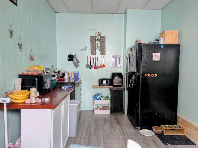 kitchen with black fridge, wood finished floors, range with electric stovetop, dark countertops, and white cabinetry