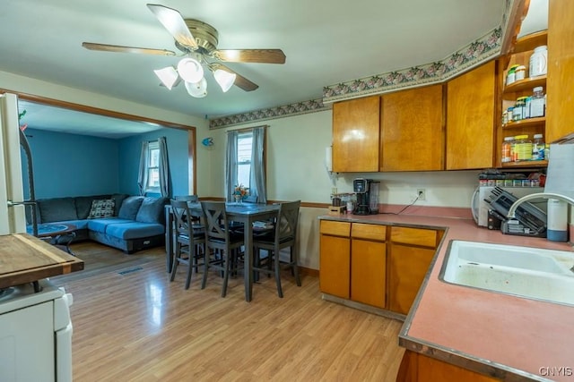 kitchen with a sink, light wood-style flooring, ceiling fan, and brown cabinets
