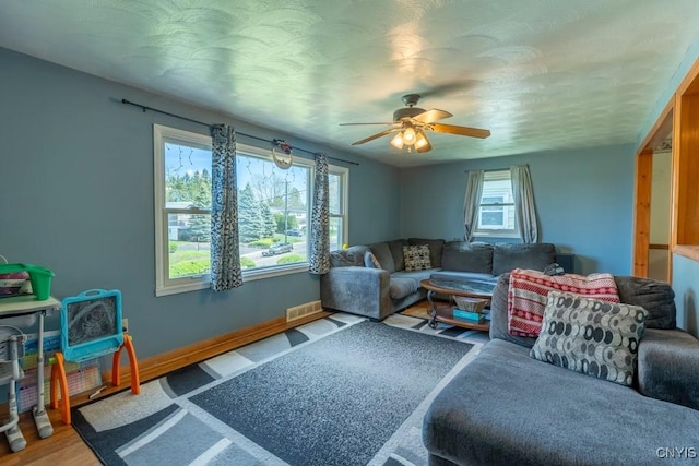 living area with baseboards, ceiling fan, and visible vents