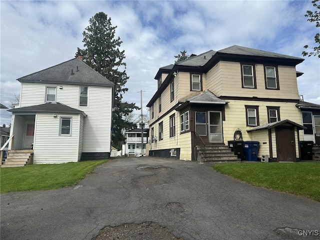 rear view of property with aphalt driveway, a shed, entry steps, a lawn, and an outdoor structure