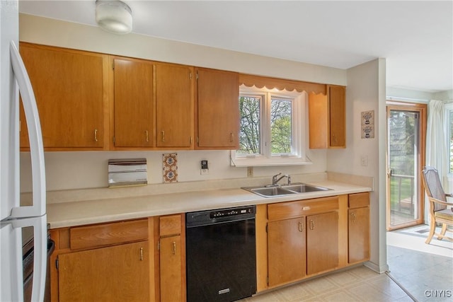 kitchen with brown cabinetry, freestanding refrigerator, black dishwasher, light countertops, and a sink