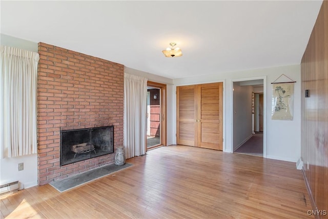 unfurnished living room with visible vents, light wood-style floors, a brick fireplace, and baseboards