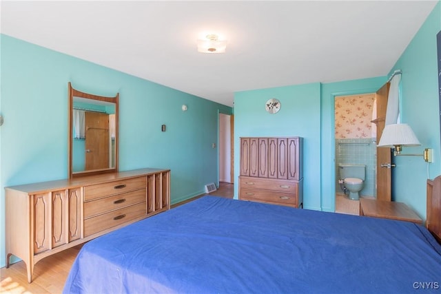 bedroom with connected bathroom, visible vents, and wood finished floors