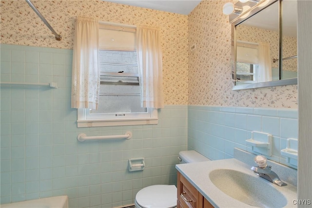 full bath with wainscoting, tile walls, toilet, and wallpapered walls