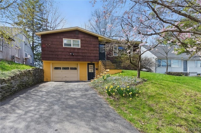 tri-level home featuring aphalt driveway, a front yard, stucco siding, an attached garage, and stairway