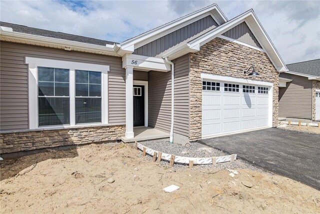 view of front of house with board and batten siding, an attached garage, driveway, and stone siding