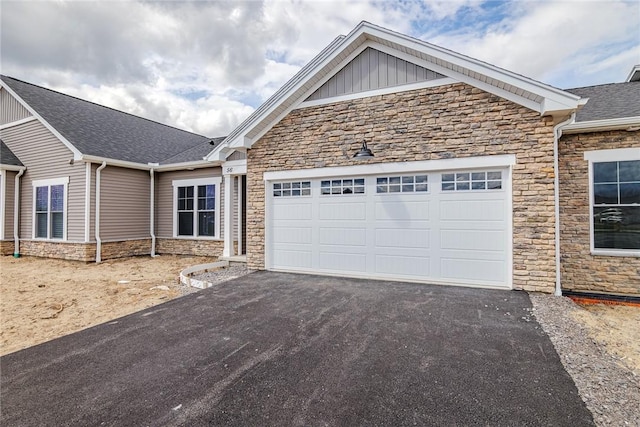 single story home with an attached garage, board and batten siding, driveway, and stone siding