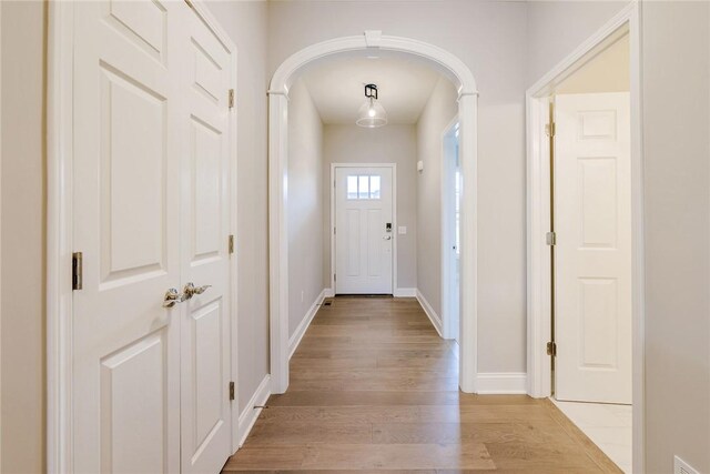 doorway to outside with arched walkways, baseboards, and light wood-style flooring