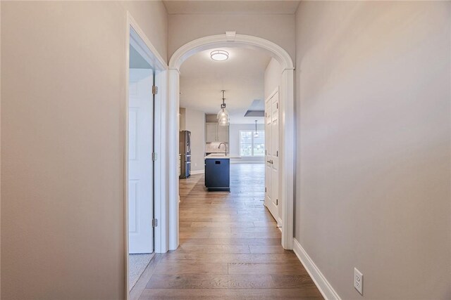 hallway featuring wood-type flooring, arched walkways, baseboards, and a sink