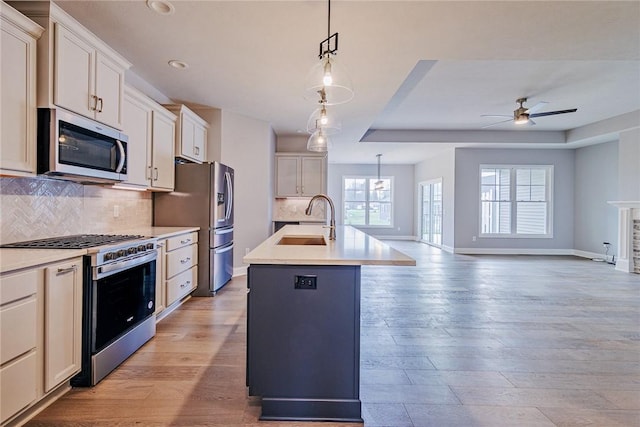 kitchen with a sink, light countertops, stainless steel appliances, a ceiling fan, and a center island with sink