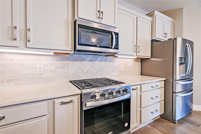 kitchen with white cabinets, appliances with stainless steel finishes, light wood-style flooring, and light stone counters