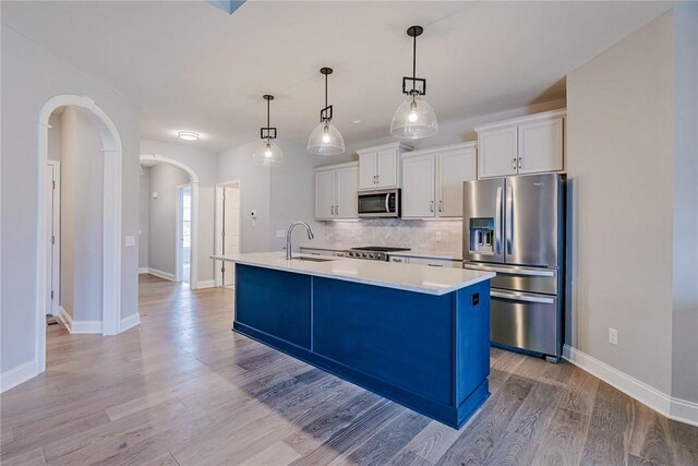 kitchen featuring a sink, an island with sink, tasteful backsplash, arched walkways, and appliances with stainless steel finishes