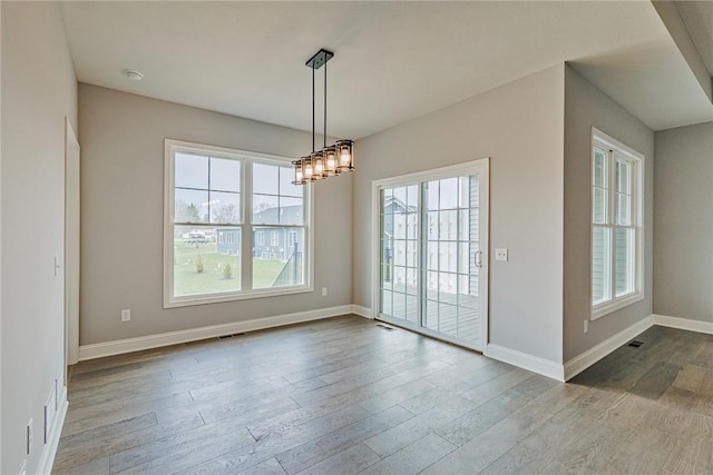 unfurnished dining area with baseboards, a chandelier, wood finished floors, and visible vents