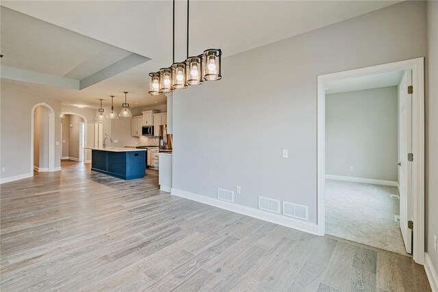 kitchen with appliances with stainless steel finishes, a sink, light wood finished floors, open floor plan, and visible vents