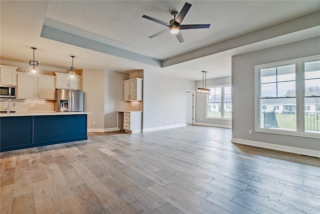 unfurnished living room with a sink, baseboards, a ceiling fan, and light wood-type flooring