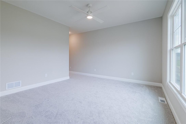 carpeted spare room with visible vents, a ceiling fan, and baseboards