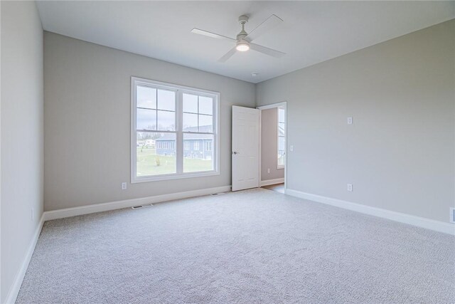 carpeted spare room with visible vents, baseboards, and ceiling fan