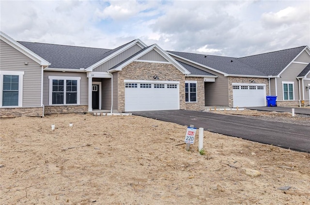 view of front of property featuring a shingled roof, an attached garage, driveway, and stone siding