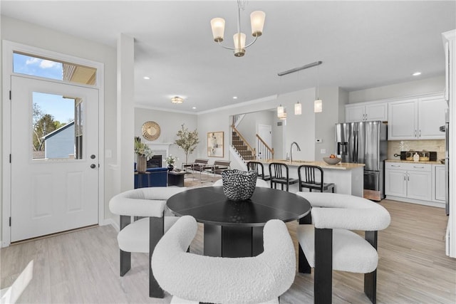 dining room featuring a fireplace, stairway, light wood finished floors, a notable chandelier, and recessed lighting