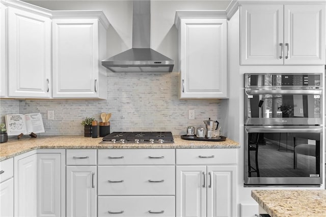 kitchen with decorative backsplash, white cabinets, wall chimney range hood, and stainless steel appliances