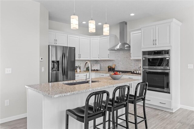 kitchen featuring appliances with stainless steel finishes, a sink, wall chimney exhaust hood, baseboards, and tasteful backsplash