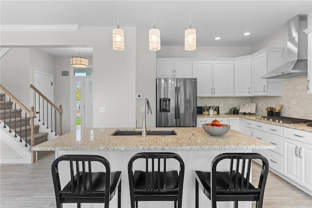 kitchen with wall chimney range hood, decorative backsplash, appliances with stainless steel finishes, light wood-type flooring, and a sink