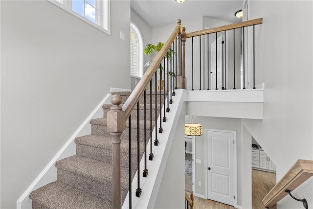 stairway with baseboards, a towering ceiling, and wood finished floors
