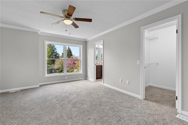 unfurnished bedroom featuring a walk in closet, ornamental molding, light carpet, and baseboards