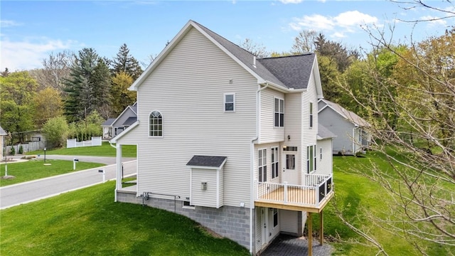back of property with roof with shingles, a wooden deck, and a yard