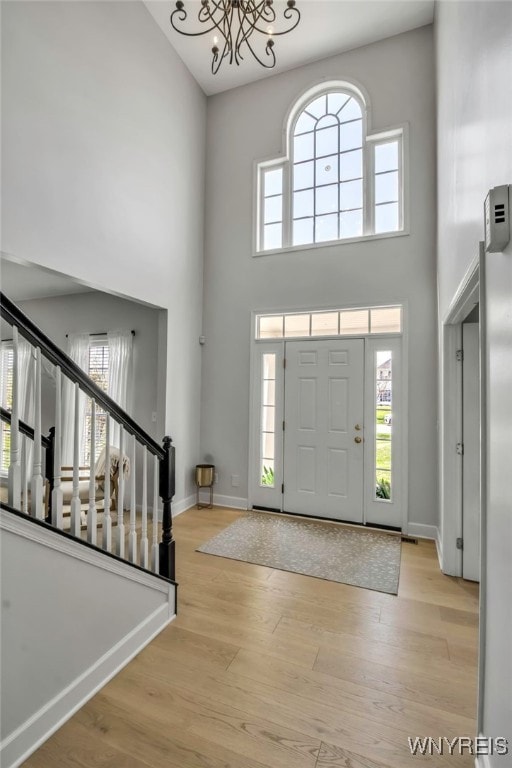 foyer entrance featuring baseboards, a notable chandelier, wood finished floors, and a towering ceiling