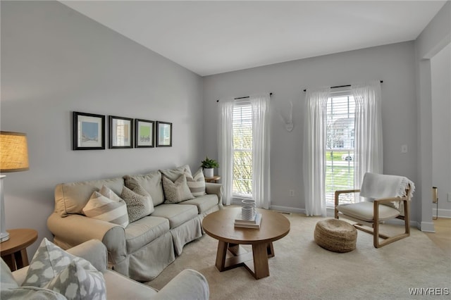 living area featuring baseboards, plenty of natural light, and light carpet