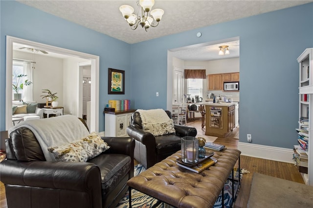 living area with baseboards, a textured ceiling, an inviting chandelier, and wood finished floors
