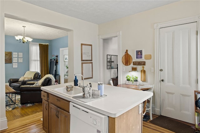 kitchen featuring light countertops, a chandelier, a sink, light wood-style flooring, and dishwasher
