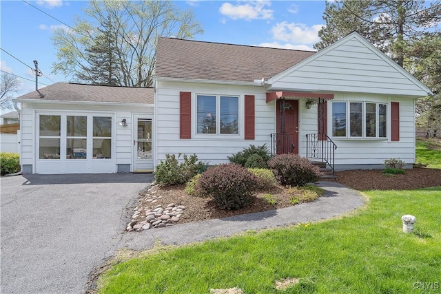 view of front of property featuring roof with shingles, a front yard, and aphalt driveway