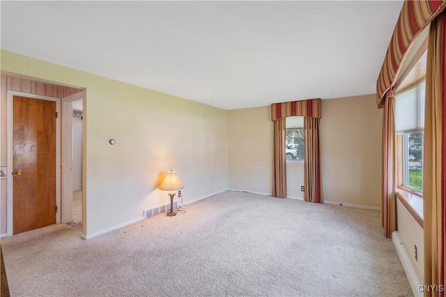empty room with baseboards, visible vents, and light carpet