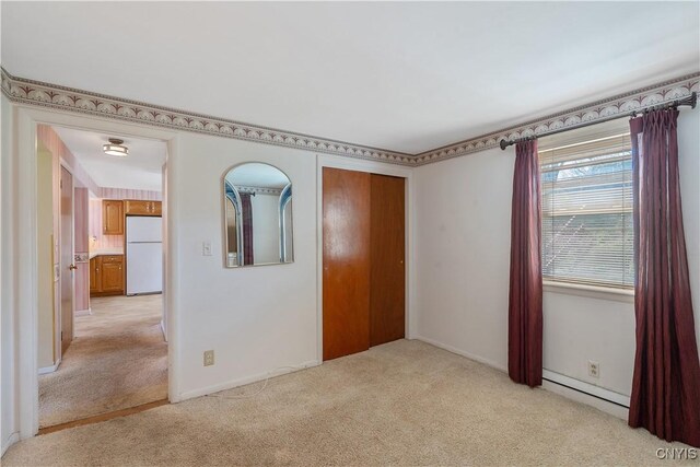 unfurnished bedroom featuring light colored carpet, baseboards, a baseboard radiator, freestanding refrigerator, and a closet