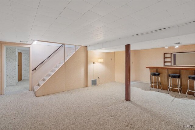 finished below grade area featuring carpet flooring, visible vents, a dry bar, and stairs