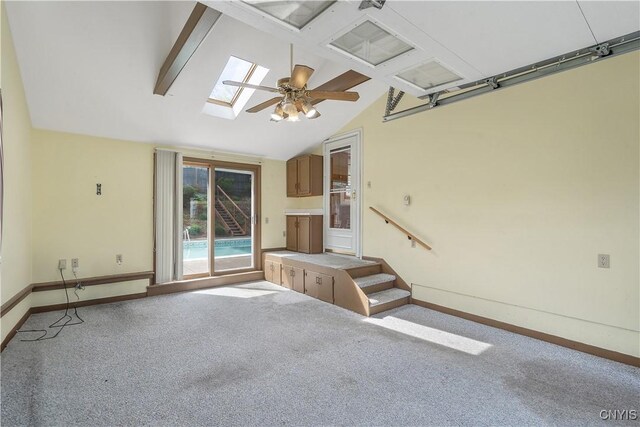 unfurnished living room featuring carpet flooring, baseboards, ceiling fan, and vaulted ceiling with skylight